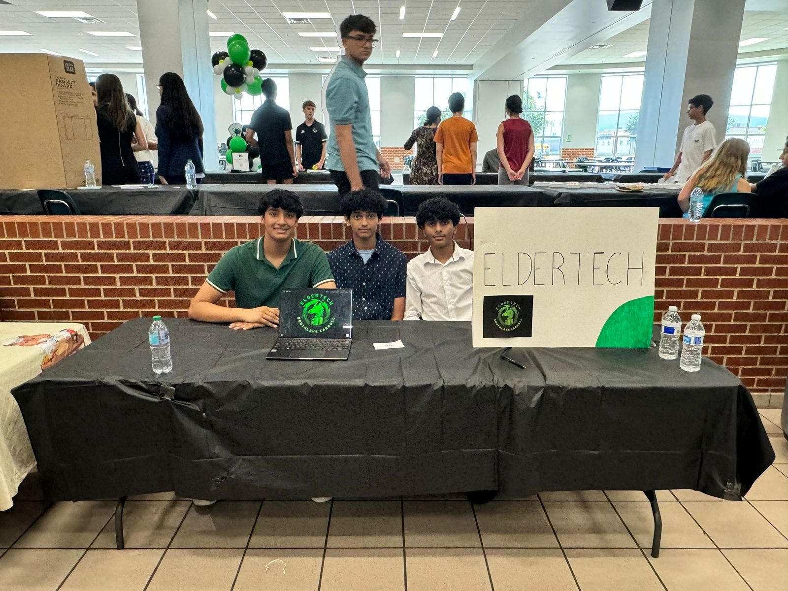 Three ElderTech students seated at their club fair table beside a hand-lettered ElderTech sign