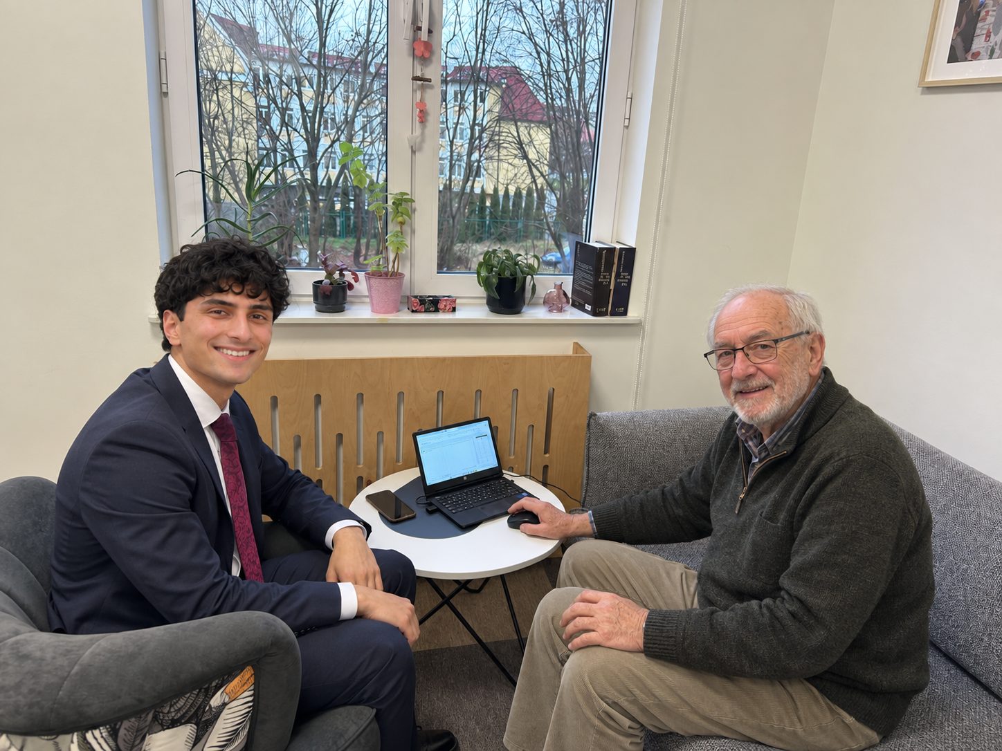 A student in a suit sitting with a smiling older man who is using a laptop
